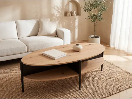Ett stilrent vardagsrum med en beigefärgad soffa och ett modernt, ovalt soffbord i trä med två hyllplan.