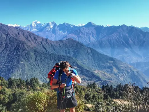 Mężczyzna z plecakiem i kijkami podczas trekkingu w Himalajach, podziwiający majestatyczne szczyty.