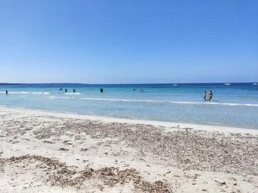 Spiaggia di Arbatax con sabbia chiara e mare cristallino, bagnanti e barche all'orizzonte. Un angolo di paradiso che ricorda la spiaggia rosa.