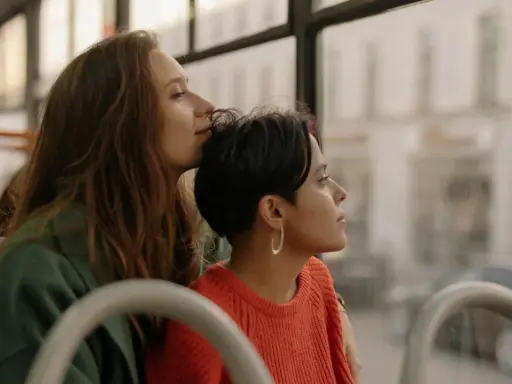 Two women share a tender moment on a bus, perhaps on their gay honeymoon, gazing out the window at the passing scenery.