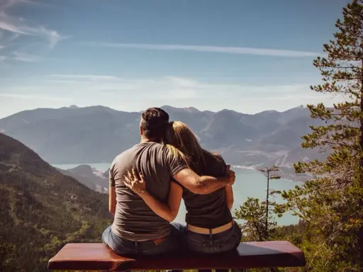 Un couple partage un moment d'amour sensuel, bras dessus, bras dessous, contemplant un paysage montagneux et un lac paisible.
