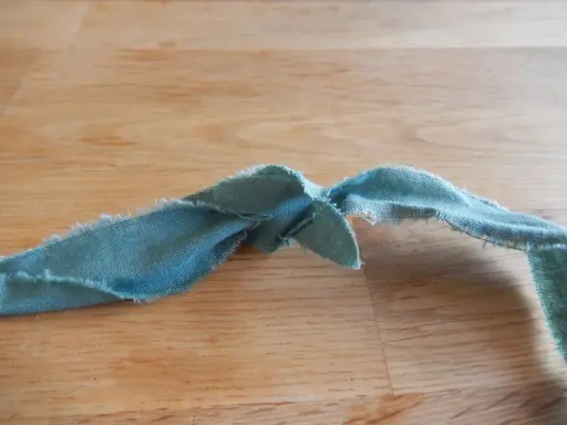 En bit tygremsa, redo att sy ihop trasmattor. Trådar hänger löst från kanterna.