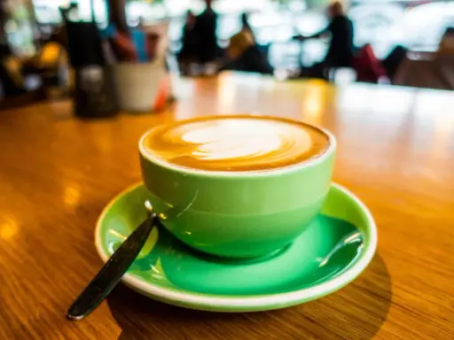 Ein cremiger Cappuccino mit doppeltem Espresso, kunstvoll verziert, in einer leuchtend grünen Tasse auf einem Holztisch.