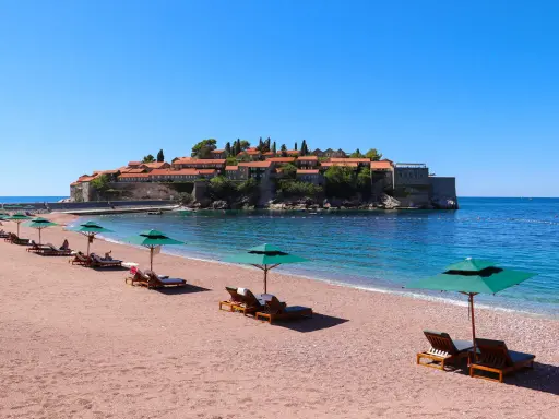 Ein idyllischer montenegro sandstrand mit Liegestühlen und Sonnenschirmen, im Hintergrund die malerische Insel Sveti Stefan.