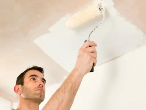Hombre pintando el techo con rodillo. Se ve la mano sujetando el rodillo y la pintura blanca aplicándose.