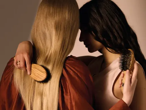 Deux femmes se serrent, l'une brosse les cheveux blonds de l'autre avec une brosse en bois.