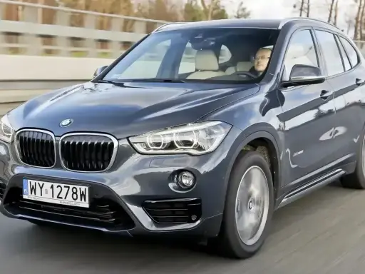 Ciemnoszary BMW X1 2025 z kierowcą za kierownicą, jadący po drodze.