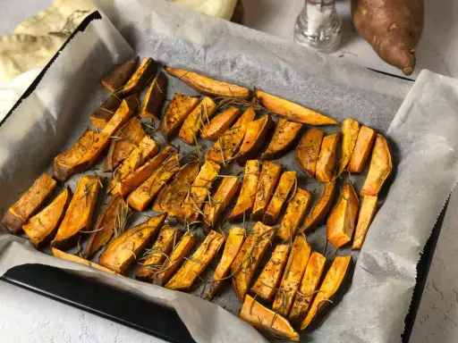 Patate dolci al forno tagliate a spicchi, condite con rosmarino e spezie, pronte per essere gustate.
