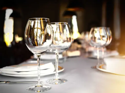 Verres à vin vides sur une table dressée, prêts pour un repas. L'emplacement verre table est soigné, reflétant la lumière ambiante.