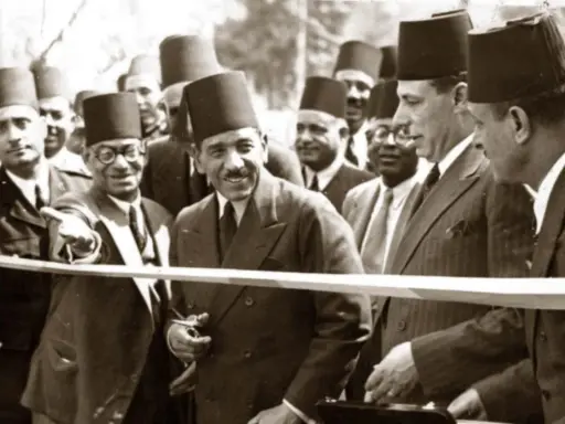 Männer in traditionellen orientalischen Filzhüten bei einer Zeremonie. Einer schneidet mit einer Schere ein Band durch.