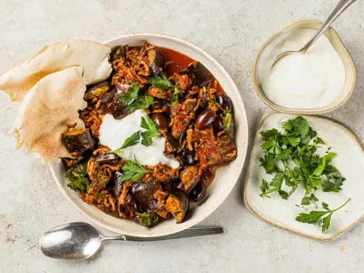 Délicieuse recette aubergine viande hachée, servie avec du pain pita, une cuillère de yaourt et du persil frais.