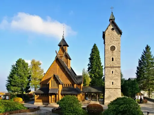 Drewniany kościółek i kamienna wieża z zegarem, jedne z głównych atrakcji Karpacz i okolice, na tle błękitnego nieba.