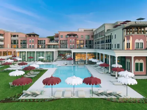 Un resort da sogno a Caorle, con piscina azzurra, lettini e ombrelloni rossi e bianchi. Un cavallino bianco potrebbe galoppare felice in questo paradiso.