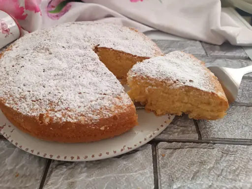 Una soffice torta al latte, spolverata di zucchero a velo, con una fetta appena tagliata pronta per essere gustata.