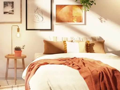 Acogedora habitación con decoración nórdica, cama con mantas y cojines cálidos, mesita de noche con planta y lámpara, y cuadros en la pared.