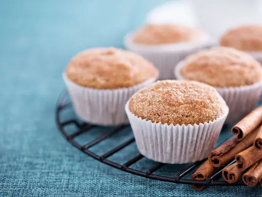 Leckere Apfelmus Muffins mit Zimt bestreut auf einem Gitter, daneben Zimtstangen.