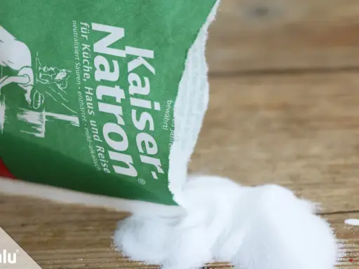 Kaiser Natron wird zum Teppich reinigen mit Natron verwendet. Das weiße Pulver liegt auf Holz.