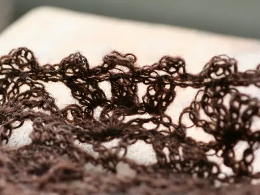 Close-up of a brown, lacy crocheted fabric with an openwork pattern.