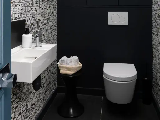 Une salle de bain moderne avec un papier peint original, un petit lavabo blanc, des serviettes roulées et une cuvette suspendue. La deco wc est soignée.