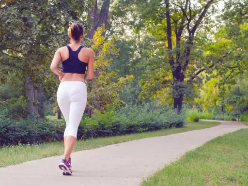 Donna corre su un sentiero nel parco, godendosi la sua zona 2 corsa tra gli alberi verdi.