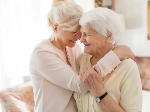 Dwie kobiety, młodsza i starsza, przytulają się. Młodsza obejmuje starszą, pokazując, jak wzmocnić starszą osobę poprzez wsparcie i bliskość.