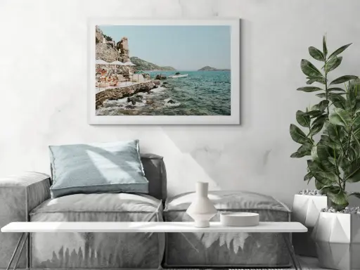 A framed print of a coastal scene, reminiscent of fine art photography galleries, hangs above a sofa. The artwork depicts a rocky shoreline with people relaxing under umbrellas.