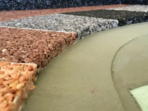 Przykładowe wykończenie tarasu betonowego: próbki nawierzchni z kamienia naturalnego w różnych kolorach, obok zielonej, gładkiej powierzchni.