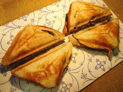 Goldbraune Bananen-Toast-Sandwiches, dreieckig geschnitten, liegen auf einem Teller mit blau-weißem Muster.