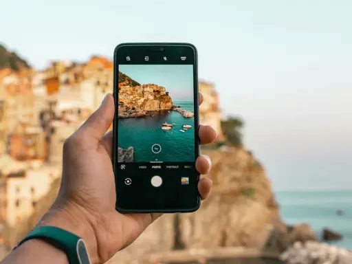 Dłoń trzyma smartfon, na ekranie którego widać malowniczą włoską wioskę nad morzem. Chcesz wiedzieć, jak ulepszyć aparat w telefonie? Oto przykład pięknego ujęcia!