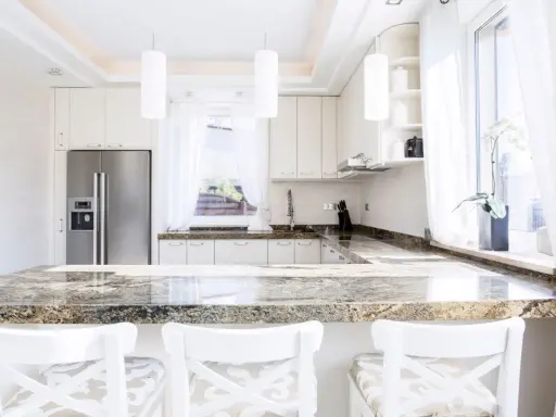 Plan de travail en granit, un danger potentiel pour les couteaux de cuisine. Cuisine moderne avec réfrigérateur, armoires blanches et tabourets.