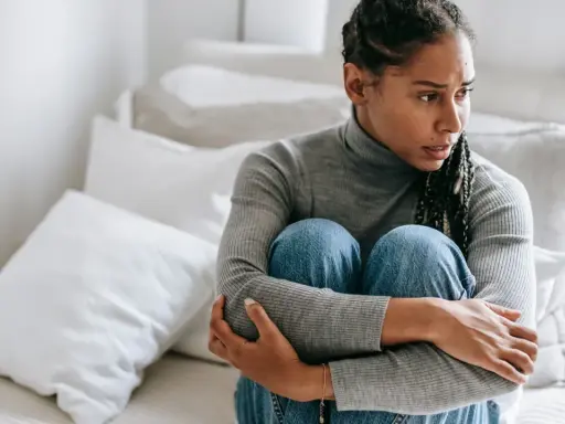 Donna seduta sul letto, abbracciata, con espressione preoccupata. Sembra soffrire di ansia da separazione dal partner.