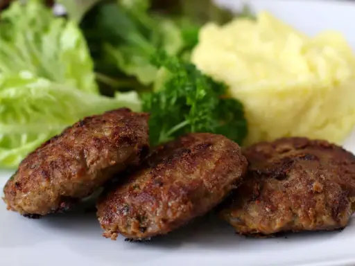 Drei gebratene Fleischpflanzerl mit Kartoffelbrei und Salat. Ein leckeres Fleischpflanzerl Rezept für zu Hause.