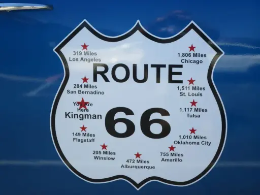 Tablica z napisem "ROUTE 66" i odległościami do miast, np. Chicago, Los Angeles, St. Louis.