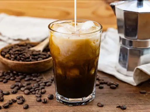 Ein Glas Eiskaffee mit Milch, Eiswürfeln und Kaffeebohnen. Perfekt für dein Cold Brew Rezept.