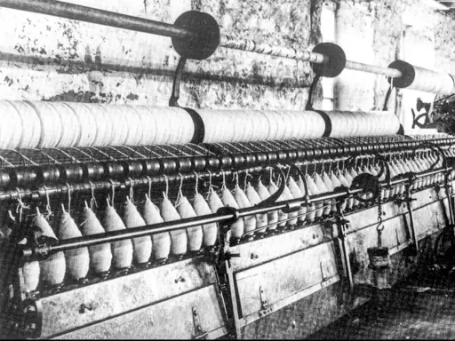 Macchinario industriale per la filatura con fili avvolti su bobine e grandi rulli.