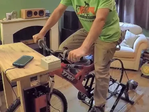 Un homme pédale sur un vélo d'appartement pour produire de l'électricité, chargeant son téléphone.