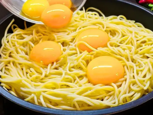 Makaron z jajkiem w patelni, żółtka tworzą złote kropki na żółtym tle.