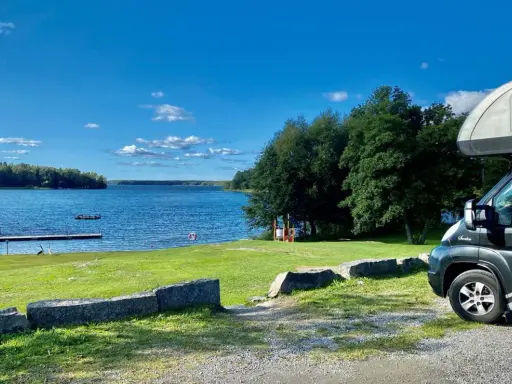 Husbil vid en sjö med brygga och gräsmatta. Perfekt för fricampa Sverige.