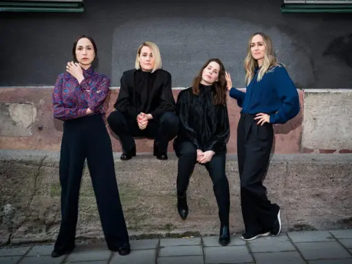Sahara Hotnights medlemmar poserar framför en vägg. De bär mörka kläder och ser ut att vara redo för en fotografering.