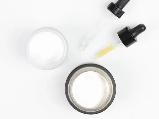 Dwa słoiczki kremu i pipetki z serum, idealne do pielęgnacji skóry głowy z kwasem salicylowym.