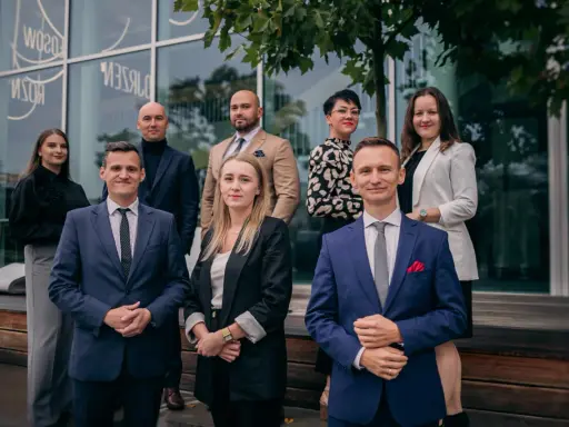 Grupa prawników w eleganckich strojach pozuje przed budynkiem.