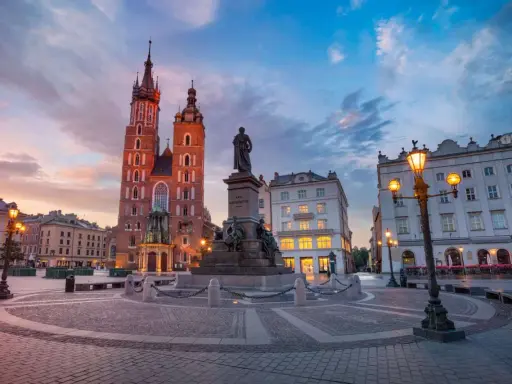 Rynek Główny w Krakowie o zachodzie słońca. Bazylika Mariacka i pomnik Mickiewicza. Ciekawe informacje o Krakowie znajdziesz w tym miejscu.