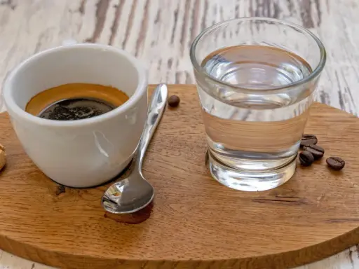 Espresso mit einem Glas Wasser, das die Aromen reinigt. Ein Keks und Kaffeebohnen vervollständigen das Bild.