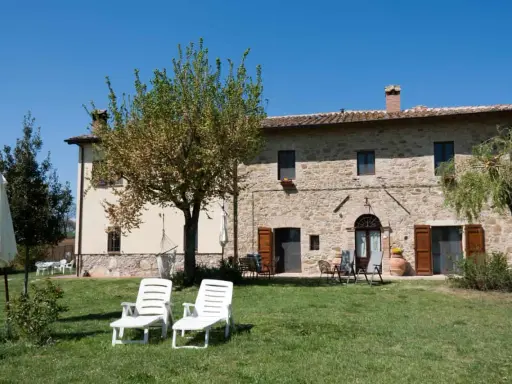 Un casale in pietra con giardino e lettini, perfetto per vacanze tranquille ad agosto in Italia.