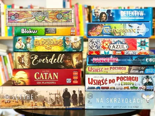 Stos gier planszowych, w tym "Sagrada", "Blokus", "El Dorado", "Everdell", "Catan", "Scythe", "Detektyw", "Carcassonne", "Azul", "Pandemic", "Wsiąść do Pociągu" i "Na Skrzydłach". Idealne gry logiczne dla dorosłych po polsku.