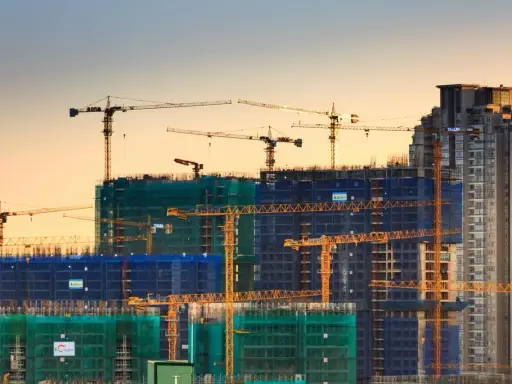 Grúas de construcción trabajando en la edificación de rascacielos, mostrando los elementos estructurales de un edificio en proceso.