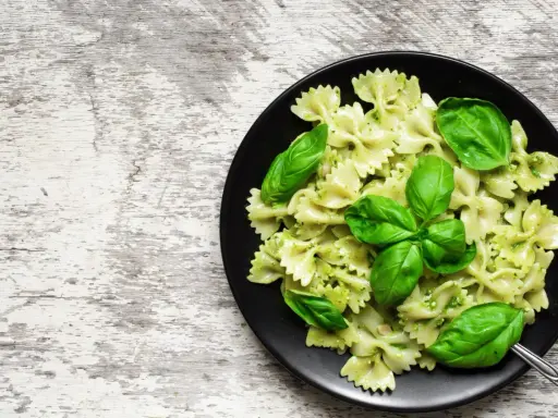 Lekkostrawny makaron farfalle z pesto i świeżą bazylią na czarnym talerzu, gotowy do podania.