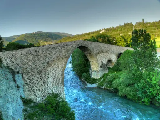 El histórico puente de San Miguel en Jaca cruza un río caudaloso rodeado de vegetación y montañas.