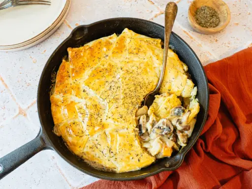 Une tourte aux champignons dorée et appétissante, servie dans une poêle en fonte, avec une cuillère prête à déguster.
