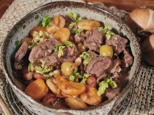 Un savoureux tajine de chevreuil mijoté avec des pommes de terre et des olives, garni de coriandre fraîche.